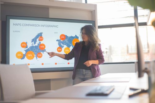 A professional woman presents an infographic comparing Europe and Asia in a bright, modern office setting.